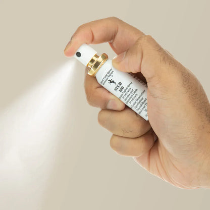 Hand holding a male desensitizer spray bottle with a beige background